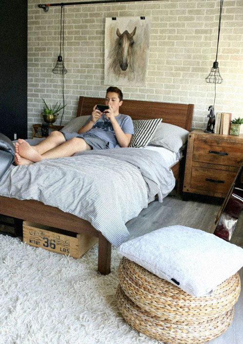 tipo rustico Com cama de madeira, parede de tijolinhos, luminárias estilo industrial e puff de vime